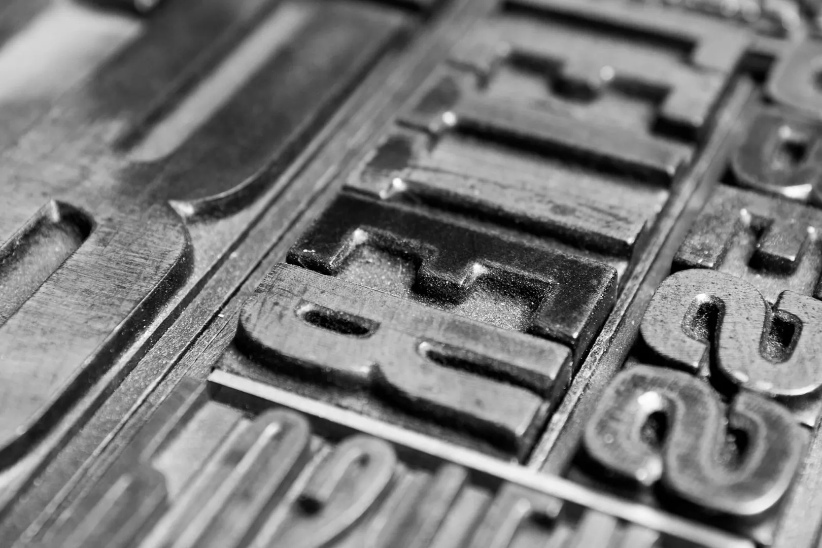 A close crop of letterpress type locked up in a chase. Each character is a separate block, cut once, held in the one position it was set in.