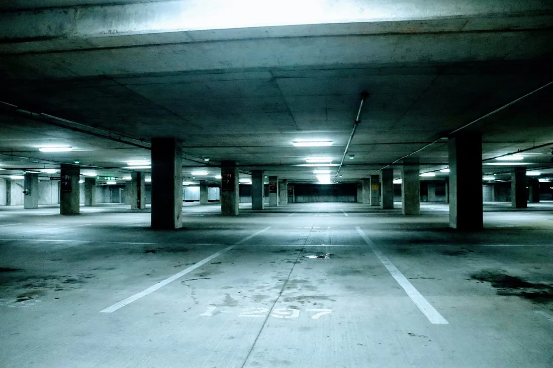A parking deck marked out into bays and standing empty, the white lines running away between the pillars under a line of ceiling lights, a number stencilled on the concrete in the foreground.
