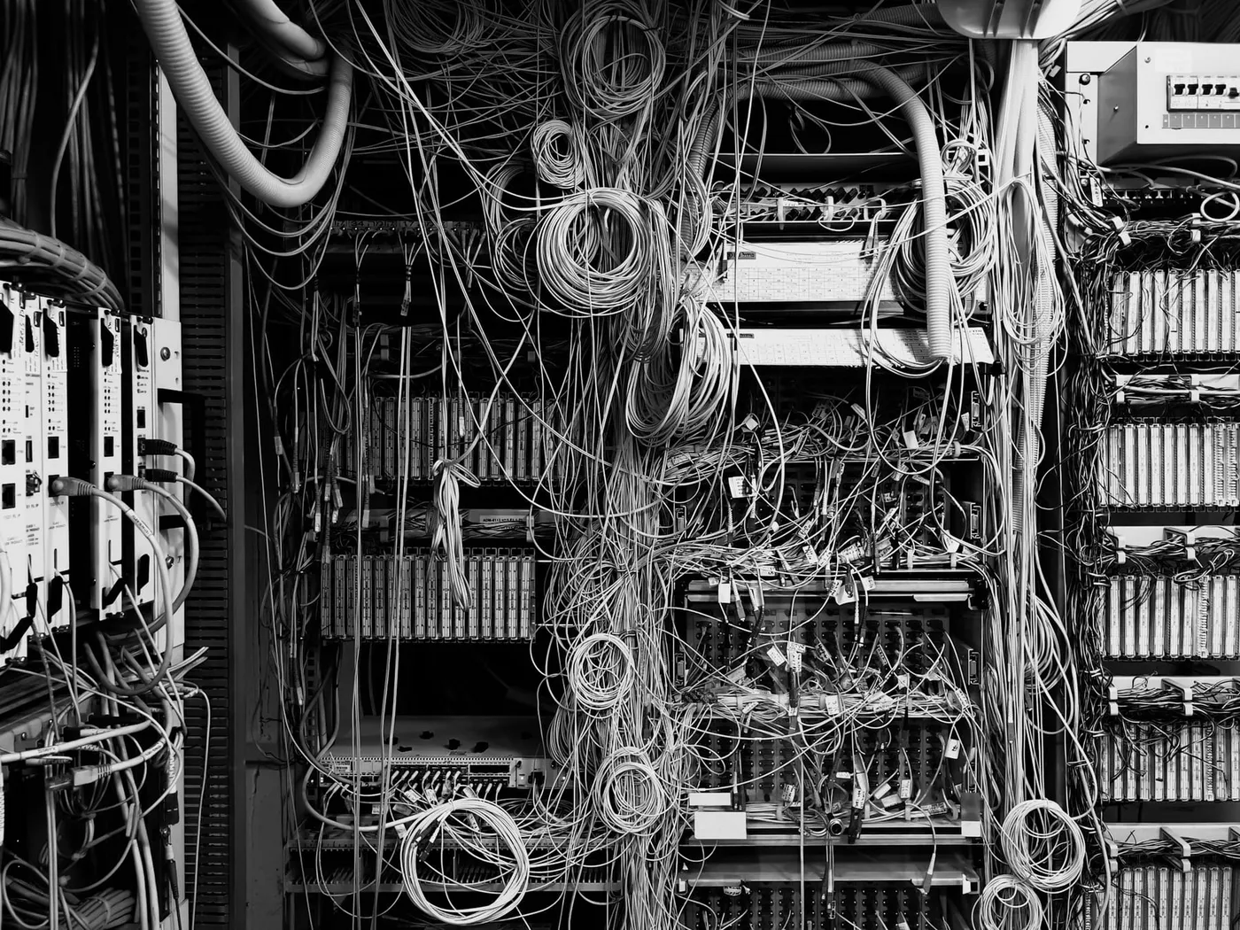A telecommunications patch cabinet with its cables running in every direction, unlabelled and crossing over one another, no route through them traceable by eye.
